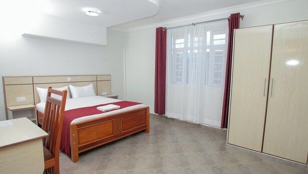 A hotel room with a wooden bed, a desk, and a wardrobe. - Hallel Guest House (Nakuru)