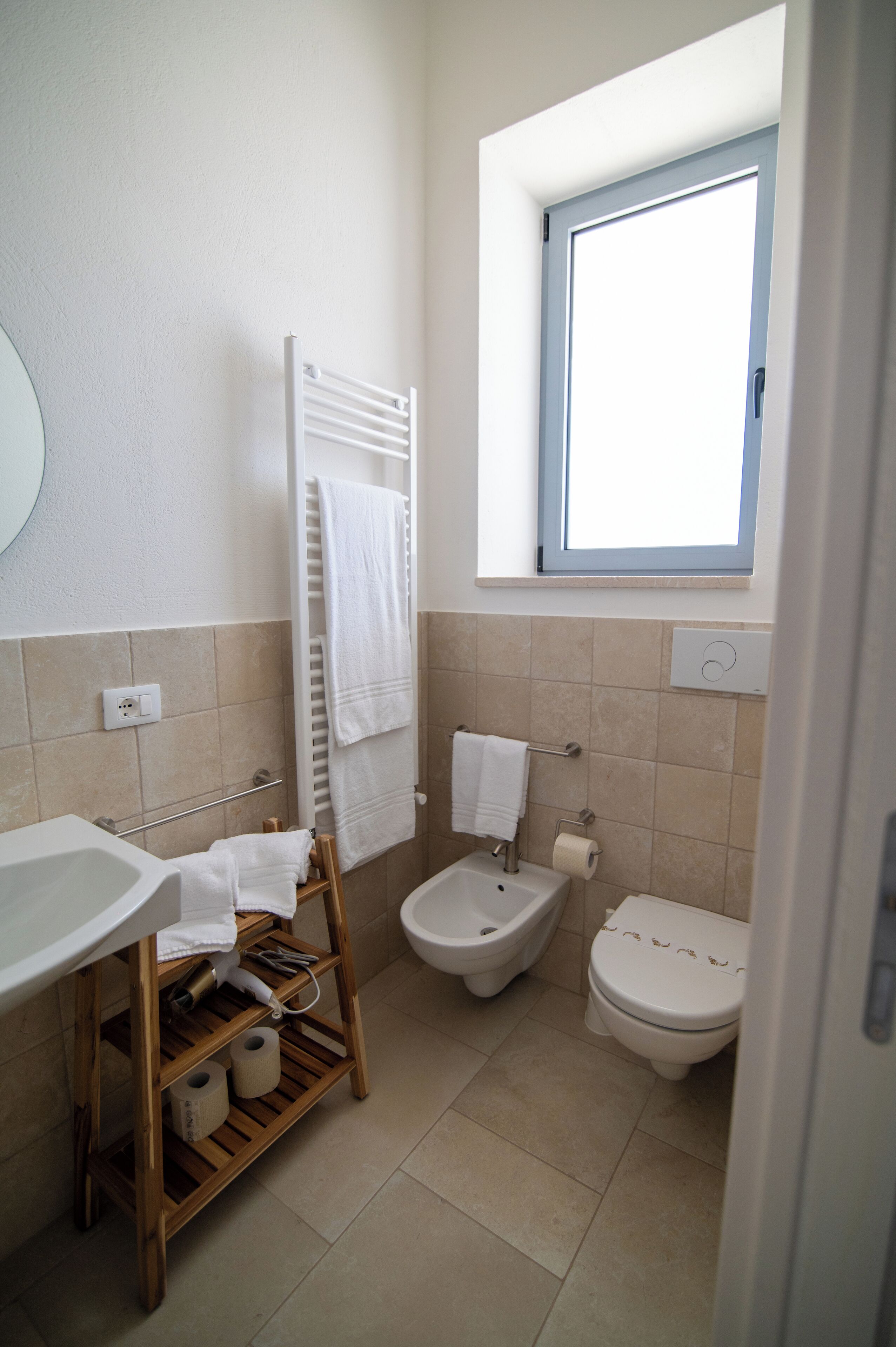 Une petite salle de bain comprenant un lavabo, des toilettes, un bidet et une fenêtre située au-dessus des toilettes.
