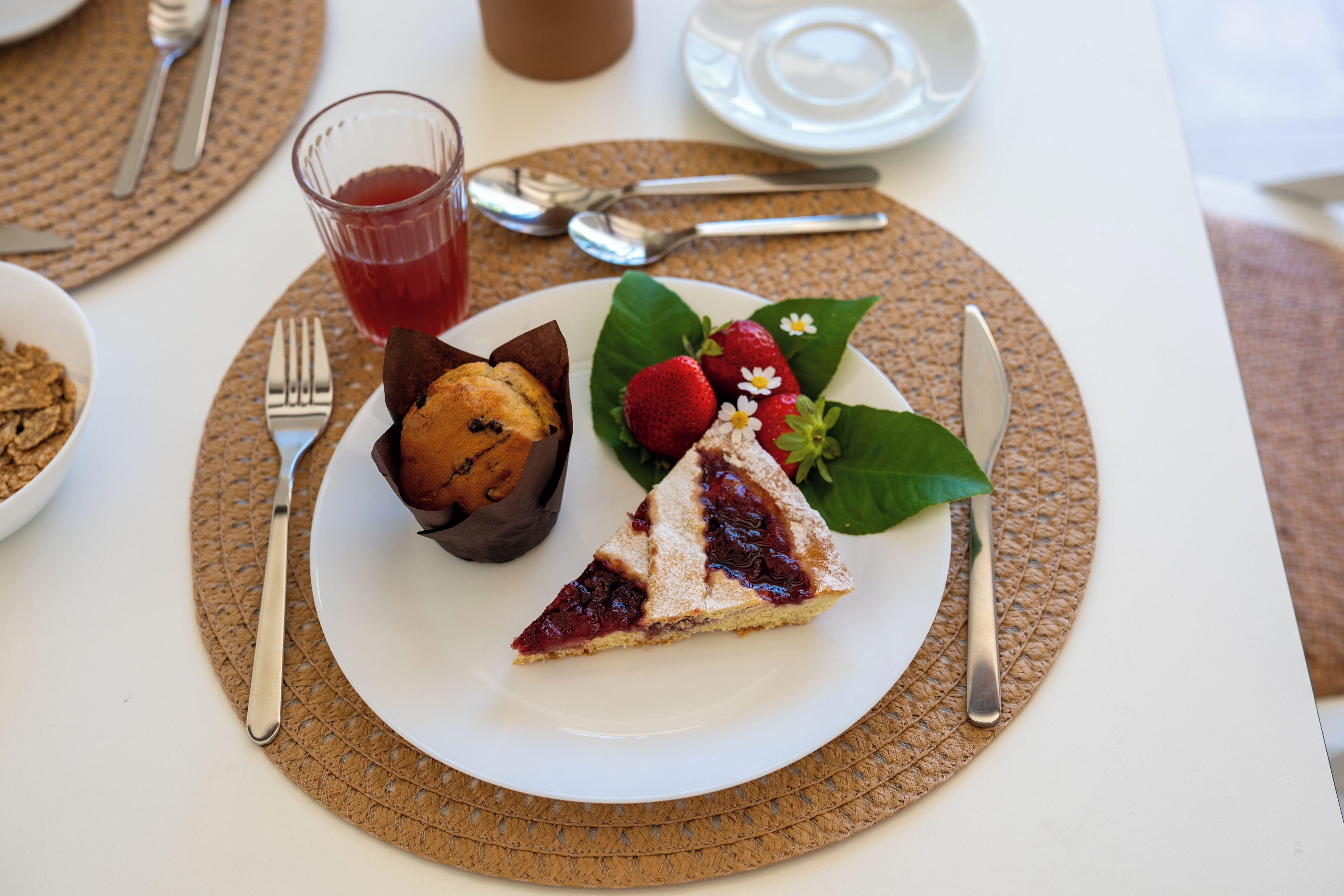 A plate with a slice of cake, strawberries, and a muffin on a placemat.