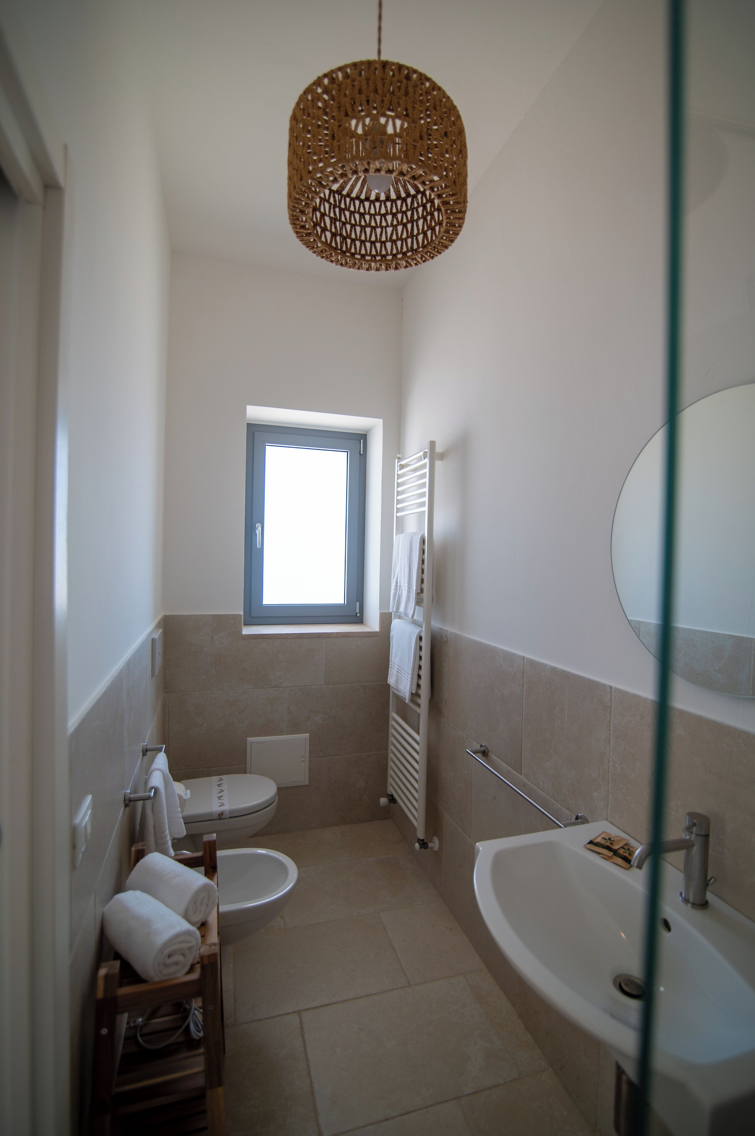 A bathroom with two toilets, a bathtub, a window, and a hanging light fixture.
