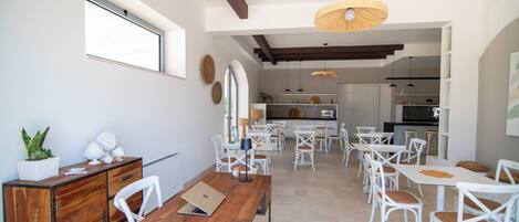 Un'ampia sala da pranzo con sedie e tavoli bianchi, un tavolo da pranzo in legno e una cucina sullo sfondo.