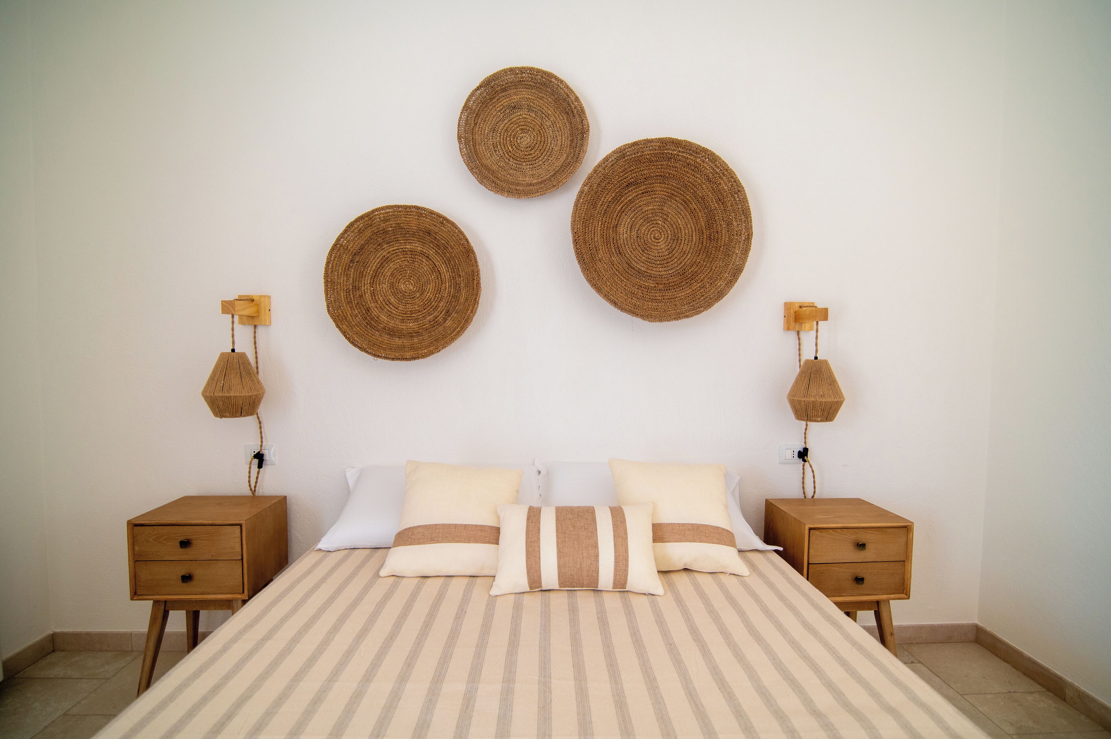 A neatly arranged bedroom with a bed, two bedside tables, and three woven wall decorations.