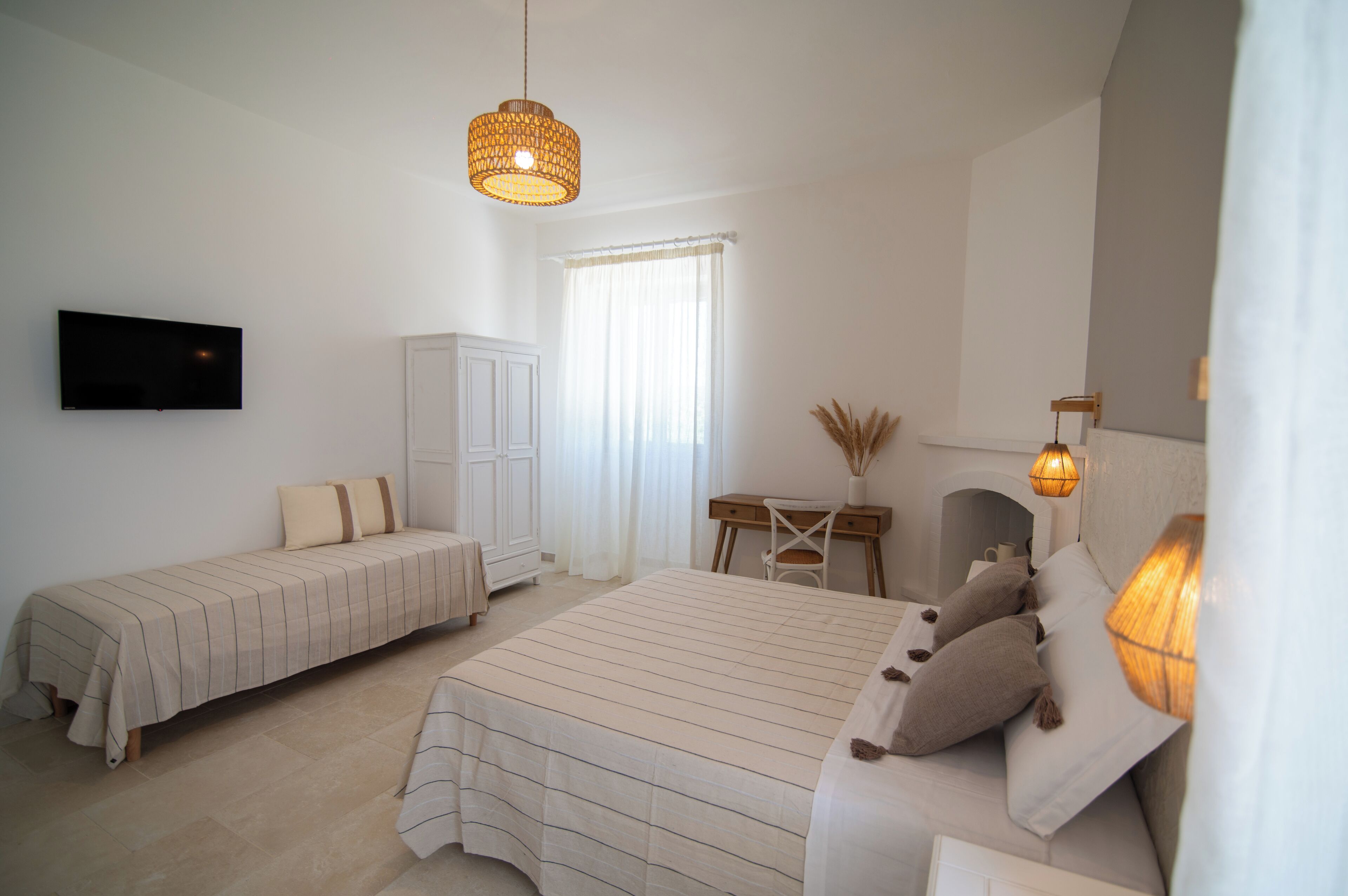 A bedroom with two beds, a TV, a desk, and a window with curtains.