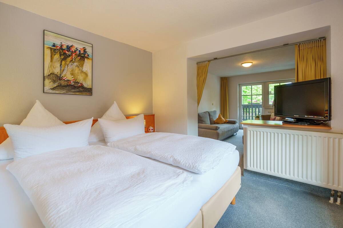 Una habitación de hotel con una cama grande, un televisor, una ventana con cortinas y un cuadro en la pared.