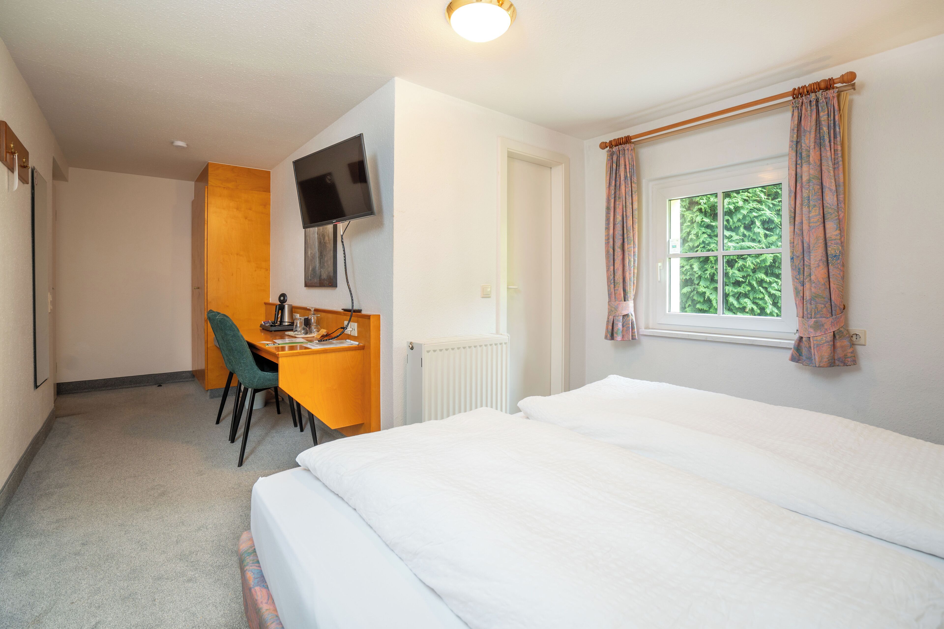 A hotel room with a bed, a desk with a chair, a television, and a window with curtains.