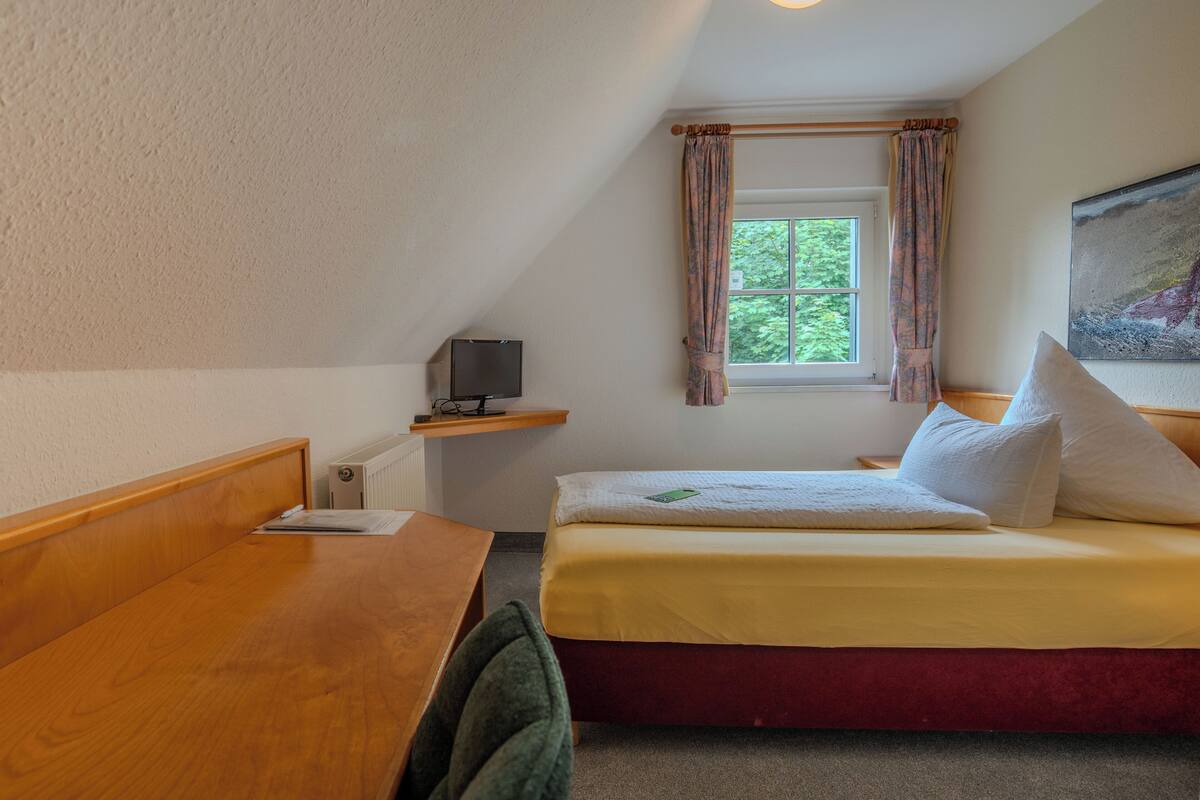 Un dormitorio con una cama de madera, un escritorio, una silla, una ventana con cortinas y un cuadro en la pared.