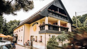 Un edificio de dos pisos con un balcón, un adorno de sol y macetas con flores.