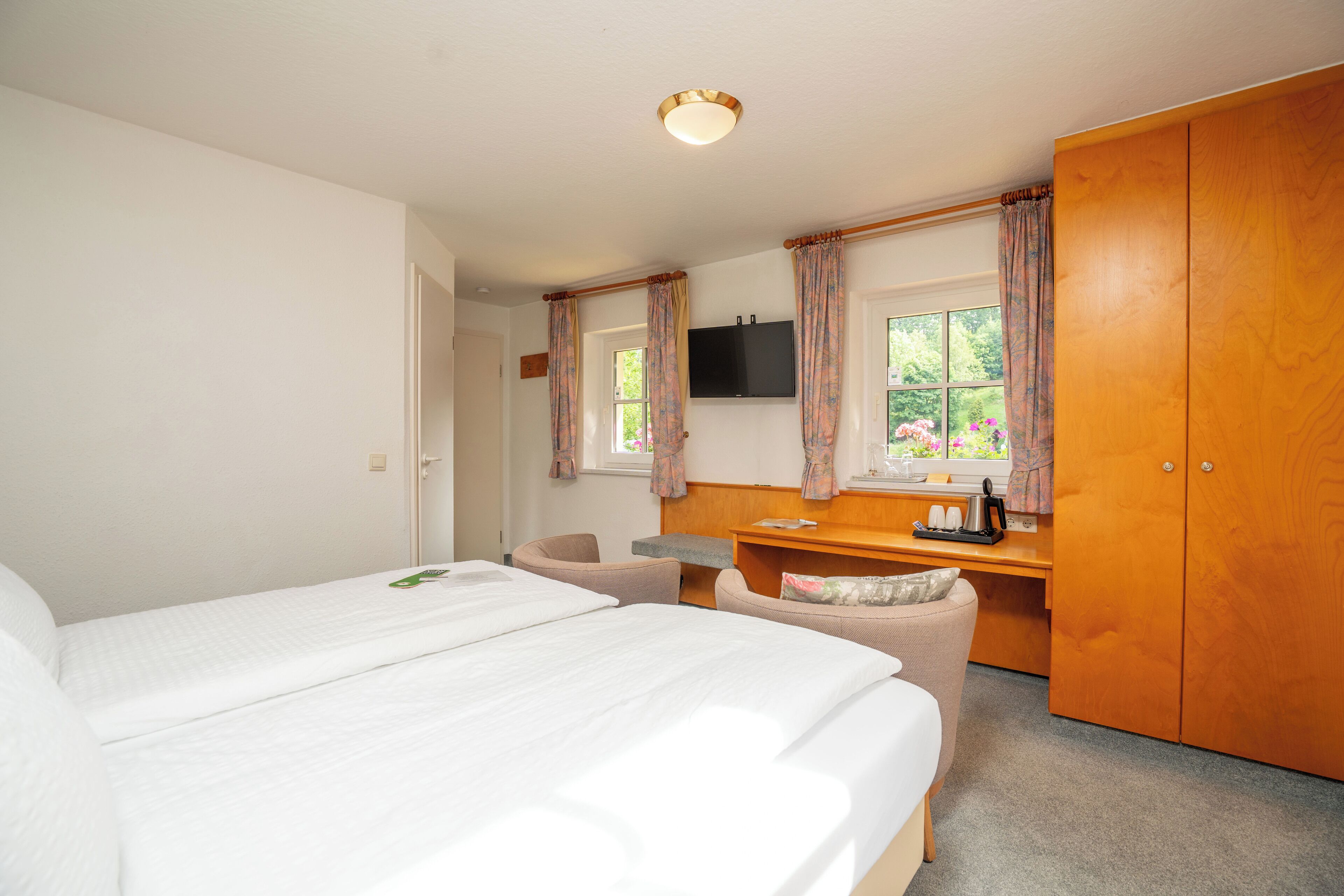 A bedroom with two beds, a desk, a chair, a wardrobe, and a television on the wall.