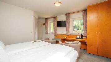 A bedroom with two beds, a desk, a chair, a wardrobe, and a television on the wall.