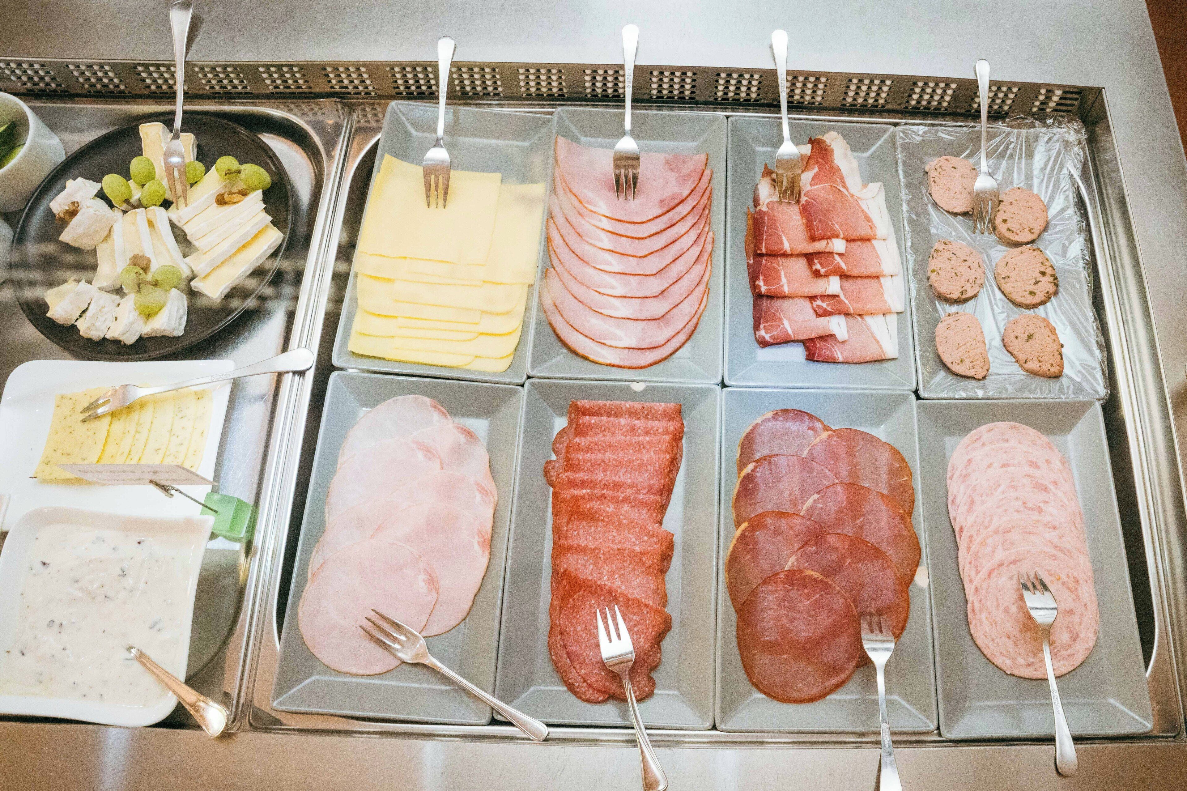 A buffet with various types of deli meats and cheeses, including ham, salami, and cheese slices, arranged on trays.