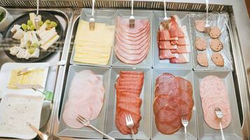 A buffet with various types of deli meats and cheeses, including ham, salami, and cheese slices, arranged on trays.