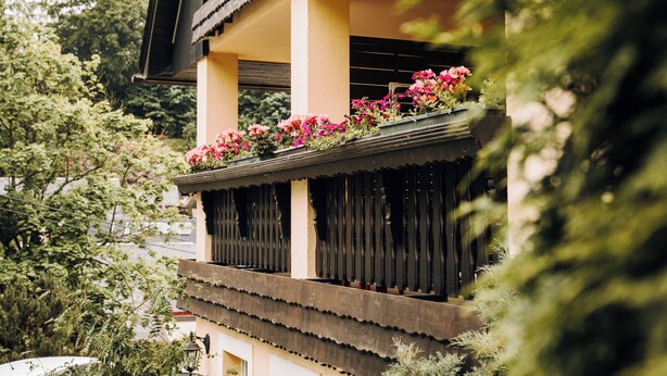 Un edificio tradicional con un balcón decorado con flores, rodeado de vegetación.