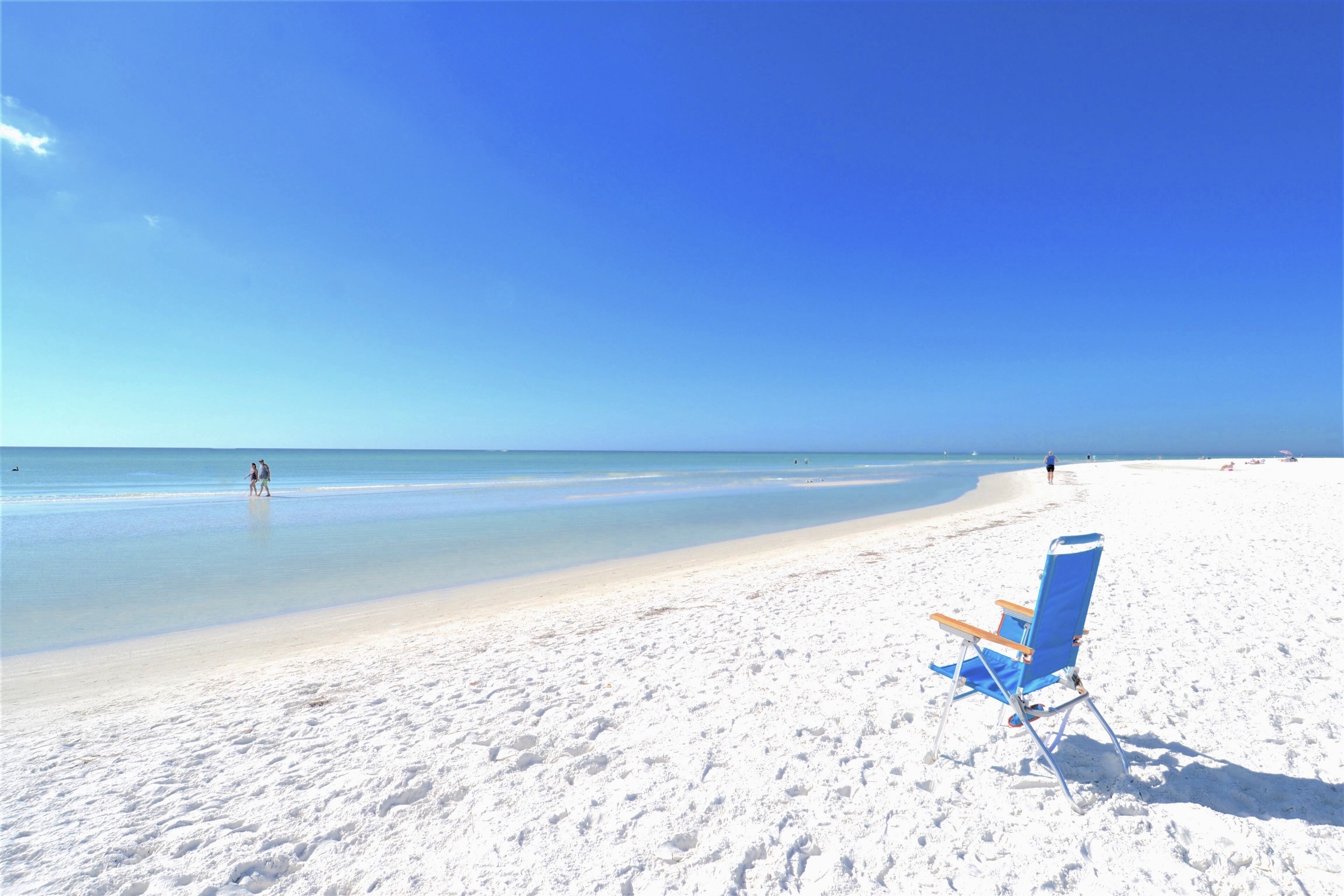Une plage avec une seule chaise longue bleue et un ciel d’un bleu limpide.