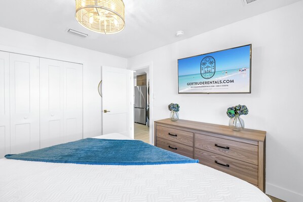 A bedroom with a bed, a blue rug, a wooden dresser, and a framed picture on the wall.