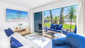 A modern living room with a white sofa, blue armchairs, and a glass door leading to a balcony with outdoor furniture. - NEW LISTING! Village Breeze - Heated Pool, Private Patio, Village and Beach! (Siesta Key)