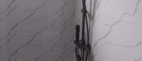 A shower with a handheld showerhead and a fixed wall-mounted showerhead, mounted on a marble wall.