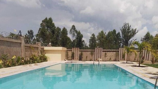 A rectangular swimming pool with clear blue water, surrounded by a tiled deck and a low stone wall. - Migori Executive Residence  (Migori)