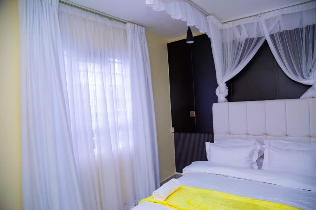 A bedroom with a bed, white curtains, and a dark headboard.
