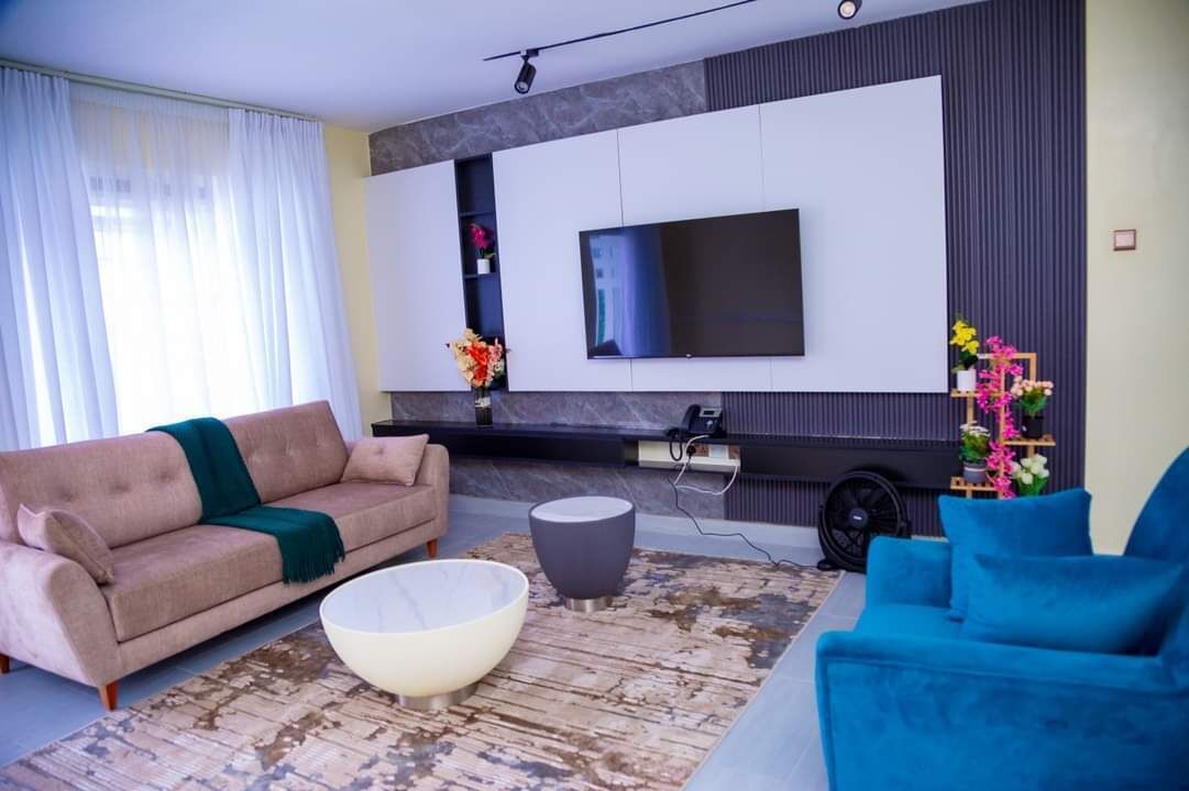 Una sala de estar moderna con un sofá color beige, un sillón azul, un tazón blanco grande y un televisor de pantalla plana montado en la pared.
