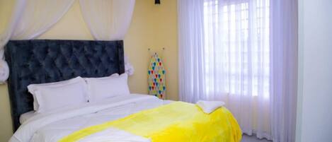 A bedroom with a bed, white curtains, and a yellow bedspread.