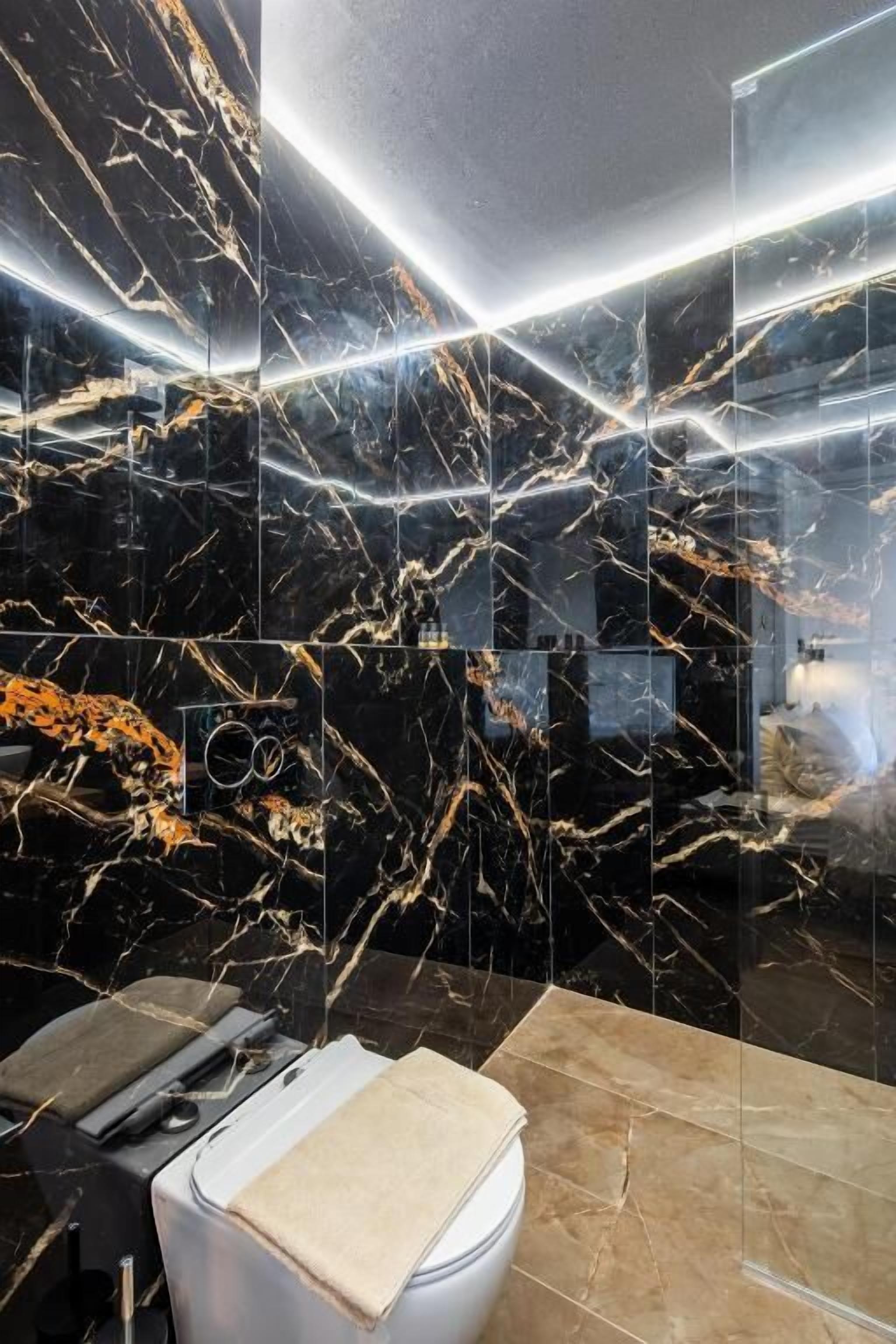 Un baño con pared de mármol negro, inodoro blanco y lavamanos con toalla color crema.