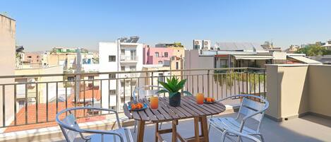 Un balcon avec une table et des chaises, un pot de fleurs et une assiette remplie d’oranges.