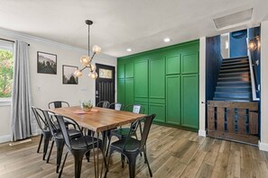 A dining area with a wooden table and chairs, a chandelier, and a green wall.