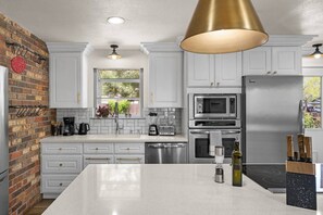A modern kitchen with white cabinetry, a central island, stainless steel appliances, and a brick accent wall.
