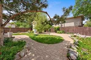 Un jardin avec une terrasse dallée, une pelouse et une clôture en bois.