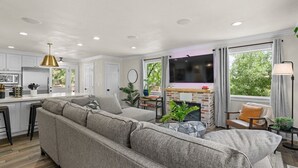 Un espacio habitable moderno con un sofá modular, una chimenea, un televisor y una zona de cocina.