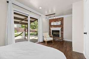 A bedroom with a large bed, a chair, a fireplace, and a sliding glass door leading to a patio.