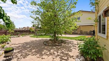 A paved courtyard with a central tree, a wooden fence, and a building with a covered patio area.