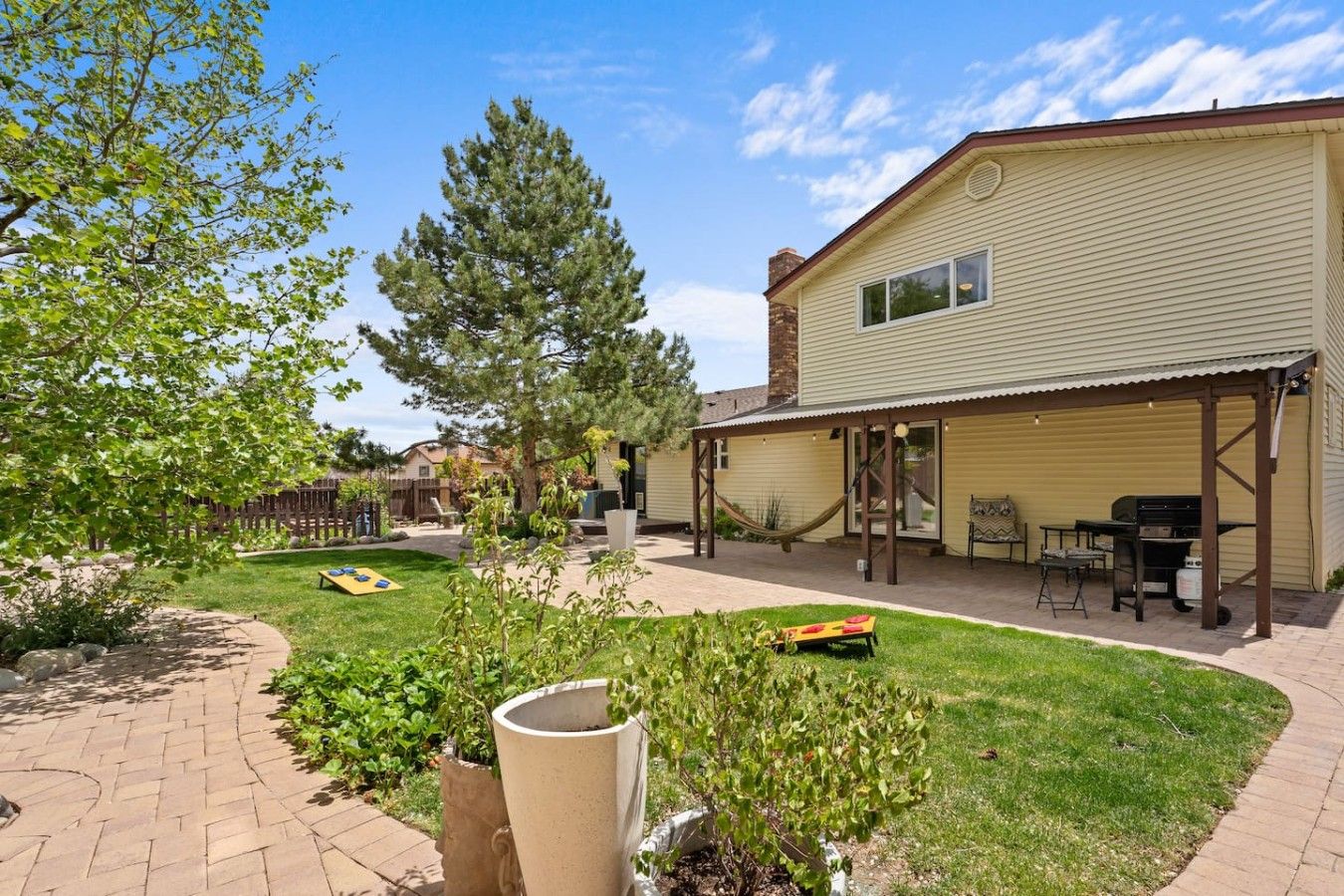 A residential backyard with a covered patio, a barbecue grill, and a hammock.