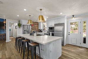 Une cuisine dotée d’un grand îlot central, d’appareils électroménagers en acier inoxydable et de luminaires suspendus.