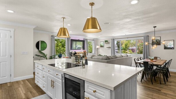 Una cocina moderna con una isla central, luces colgantes y un comedor con mesa y sillas de madera.