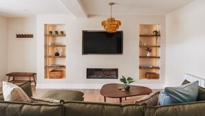 A modern living room with a large flat-screen TV, wooden shelving units, a fireplace, and a green sofa. - Ground floor apartment, central Ambleside, parking and a dog. (Ambleside)