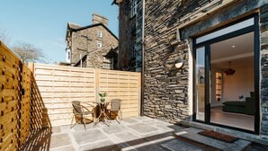 A stone building with a wooden fence, a patio with a table and chairs, and a view into a modern living space. - Ground floor apartment, central Ambleside, parking and a dog. (Ambleside)