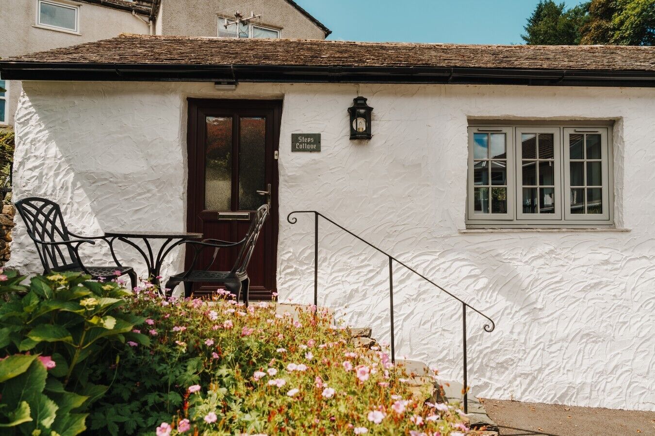 A white cottage with a dark door, a small window, and a sign reading 'Steps Cottage.'