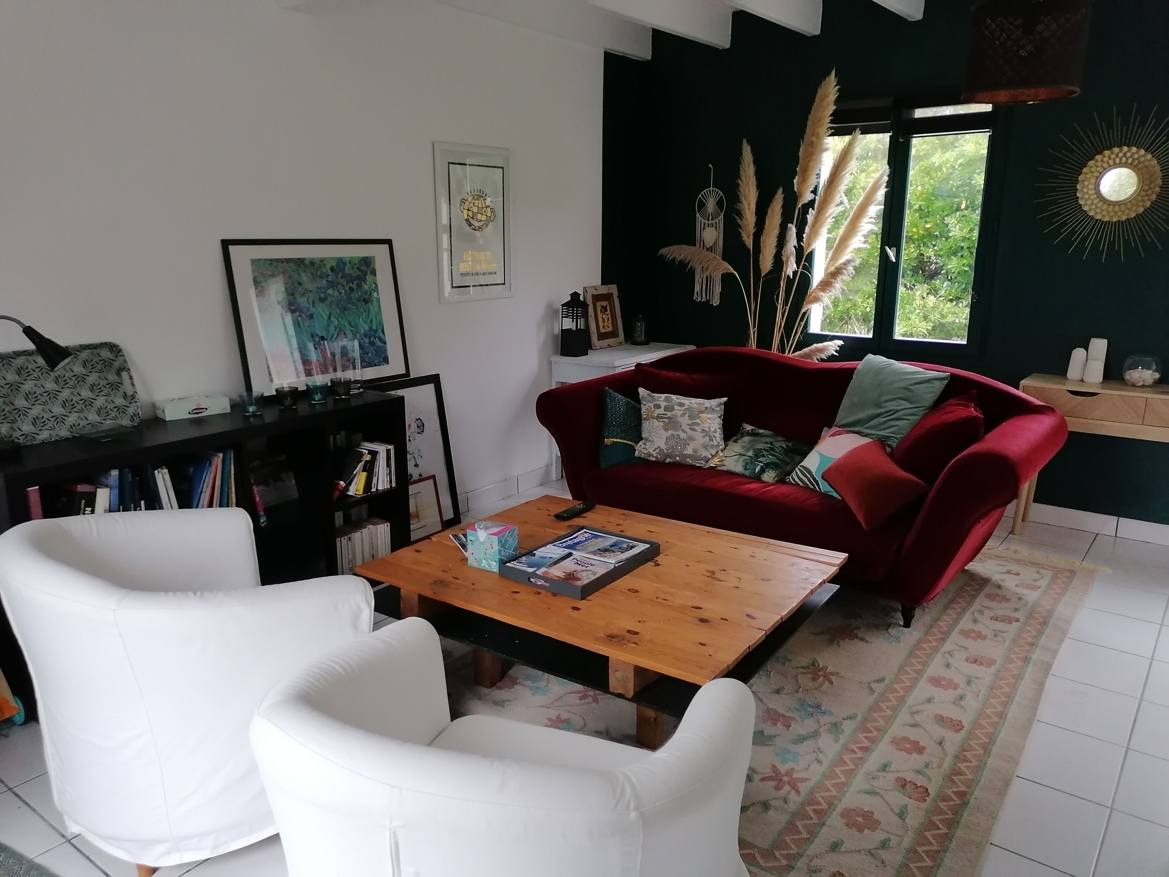 Un salon avec un canapé rouge, des fauteuils blancs, une table basse en bois et une bibliothèque.