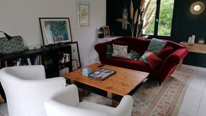 Un salon avec un canapé rouge, des fauteuils blancs, une table basse en bois et une bibliothèque.