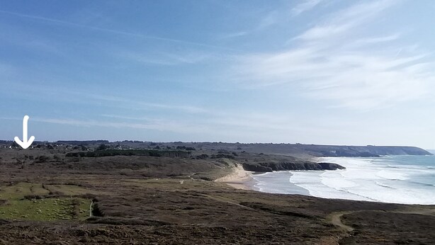 Un paysage côtier caractérisé par un relief accidenté, une plage et une ligne de côte lointaine.