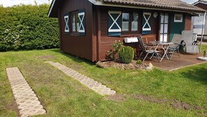 A wooden house with a tiled roof, a small garden, and a paved pathway leading to the entrance. - Vacation home for 2 people at the campsite in Wremen (Wurster Nordseeküste)