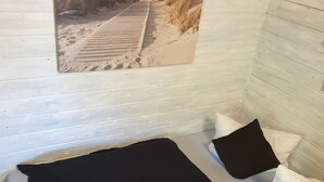 A bed with a black and white headboard, a single purple pillow, and white pillows. - Vacation home for 2 people at the campsite in Wremen (Wurster Nordseeküste)