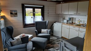 A compact kitchen with white cabinets, a dining area with two chairs, a small table, and a window with a view. - Vacation home for 2 people at the campsite in Wremen (Wurster Nordseeküste)