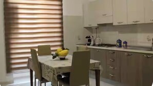 A dining area with a table set for two, a bowl of fruit, and a window with blinds.