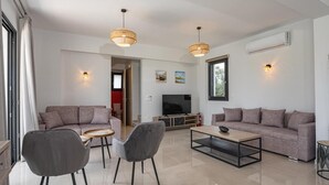 A modern living room with two sofas, a coffee table, and a TV. There are two pendant lights and an air conditioning unit on the wall.