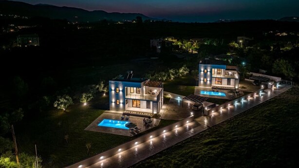 A modern two-story house with a swimming pool, surrounded by a well-lit pathway and lush greenery.