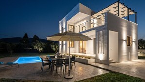 A modern two-story house with a swimming pool, outdoor seating, and a well-lit patio area.