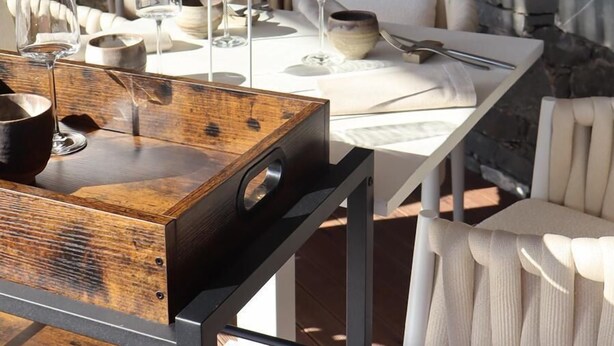 Un espace extérieur aménagé pour les repas, avec des murs en pierre, du mobilier blanc et une table en bois.