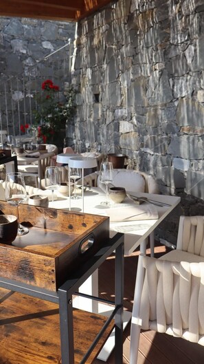 An outdoor dining area with stone walls, white furniture, and a wooden table. - Radici by Miky  (Monterosso al Mare)